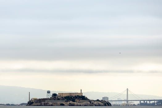 A view of Alcatraz Island with the Golden Gate Bridge in the background on a cloudy day.