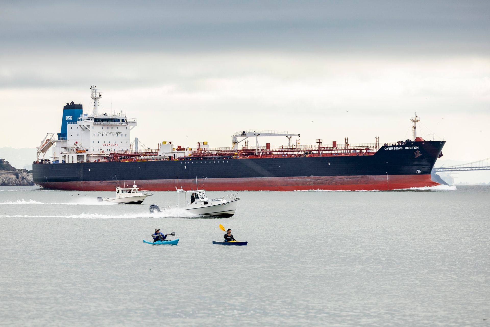Cargo ship sailing with kayakers and motorboats in the foreground.