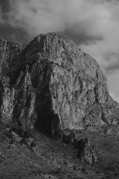 Free Dramatic black and white image of a rugged rocky mountain beneath a moody cloudy sky. Stock Photo