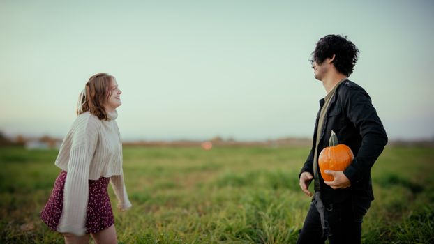 Youthful couple playing in a field holding a pumpkin during autumn.