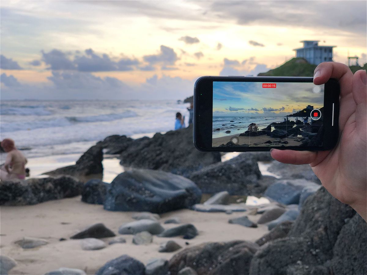 Tropikal bir plajda akıllı telefonla oturan ve ekrana bakan genç bir kişi