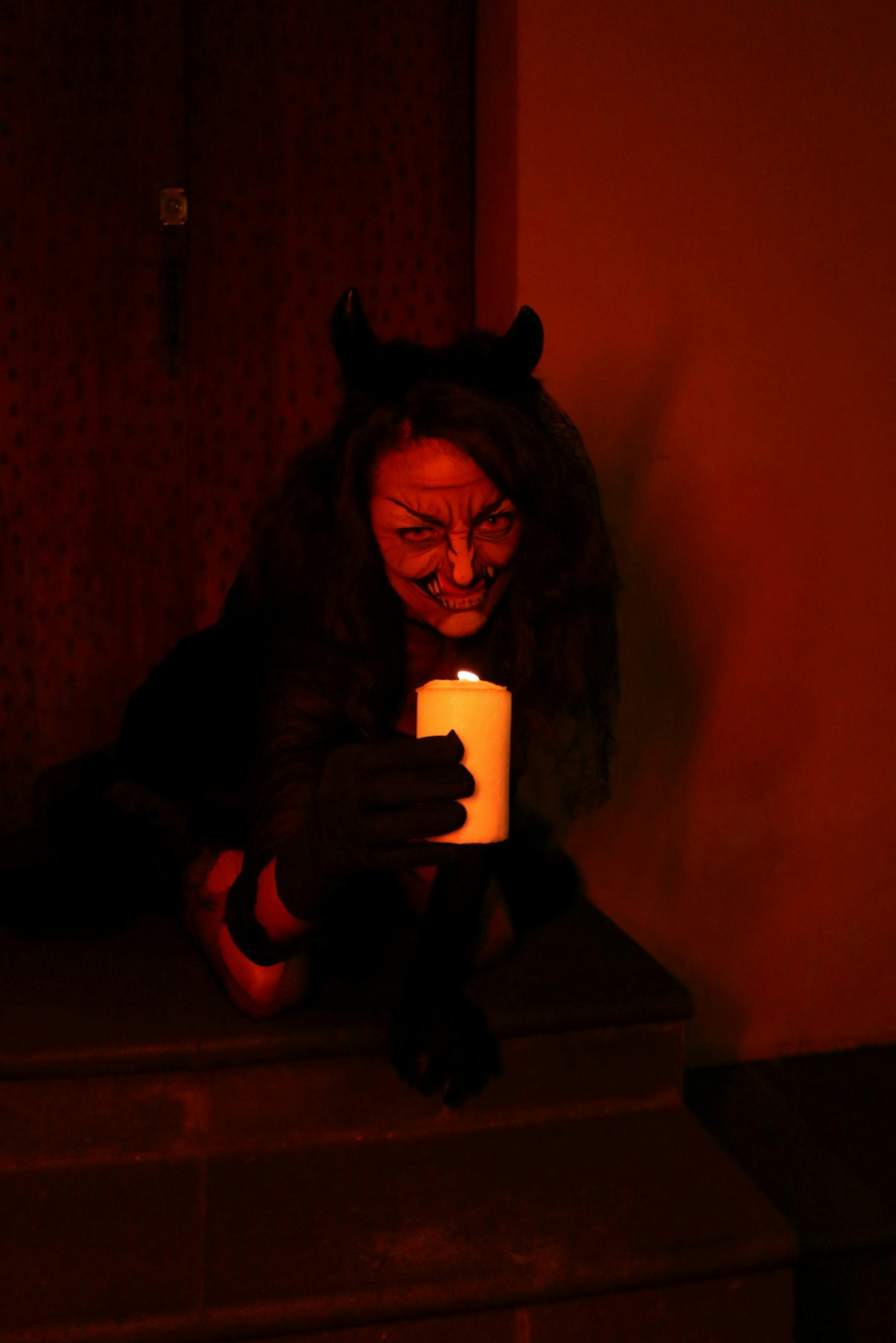 A person in dark attire holds a candle, surrounded by warm, mysterious lighting.