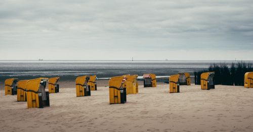 Free Serene coastal scene featuring yellow beach baskets on a sandy shore under cloudy skies at Cuxhaven, North Sea. Stock Photo
