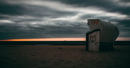 Free A captivating sunset scene on the beach with clouds and a classic beach chair, perfect for travel and nature themes. Stock Photo