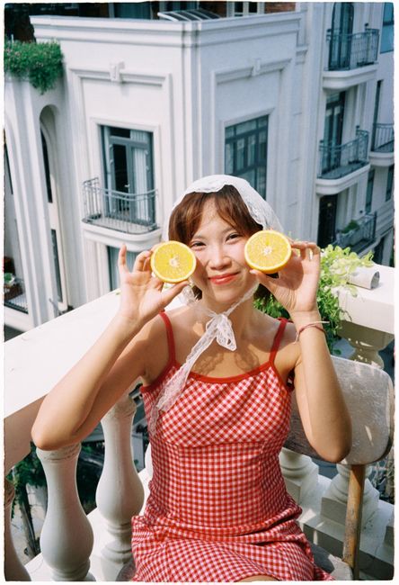 A cheerful woman holding orange slices on a sunny balcony in summer.