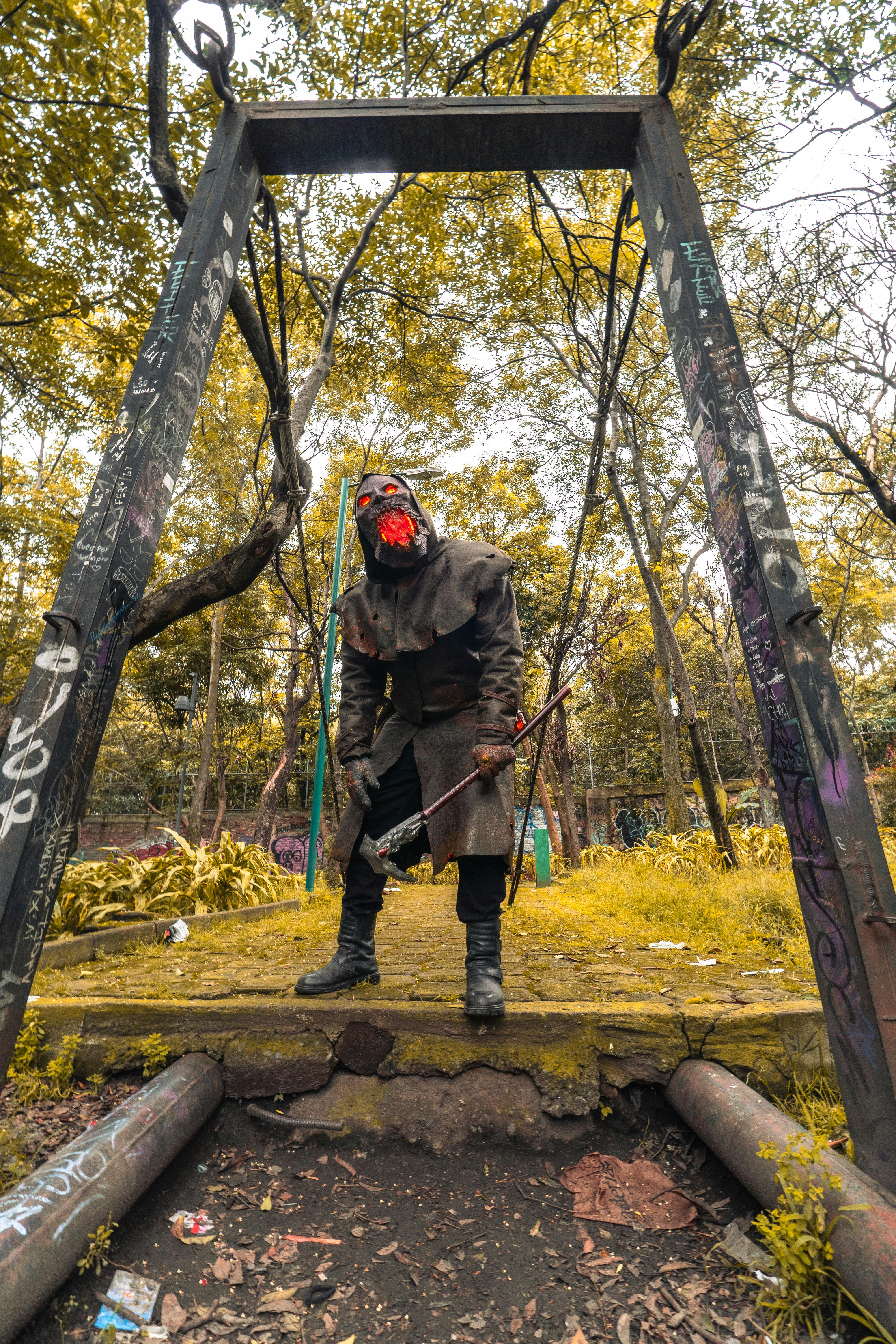 A person in a Halloween-themed cosplay costume holding a bow in a wooded area during fall.