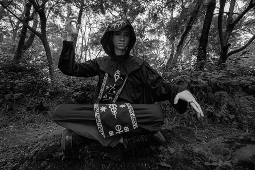 A person in mystical cosplay attire poses in a serene forest landscape.