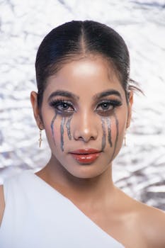 Stylish portrait of a woman with artistic, dramatic makeup and earrings against a textured background.