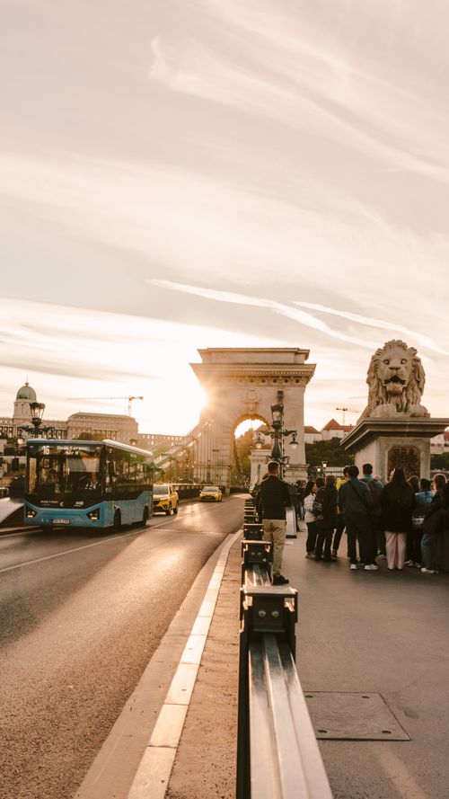 Free A scenic sunset view of Budapest's landmark Lion Bridge with people and public transport. Stock Photo
