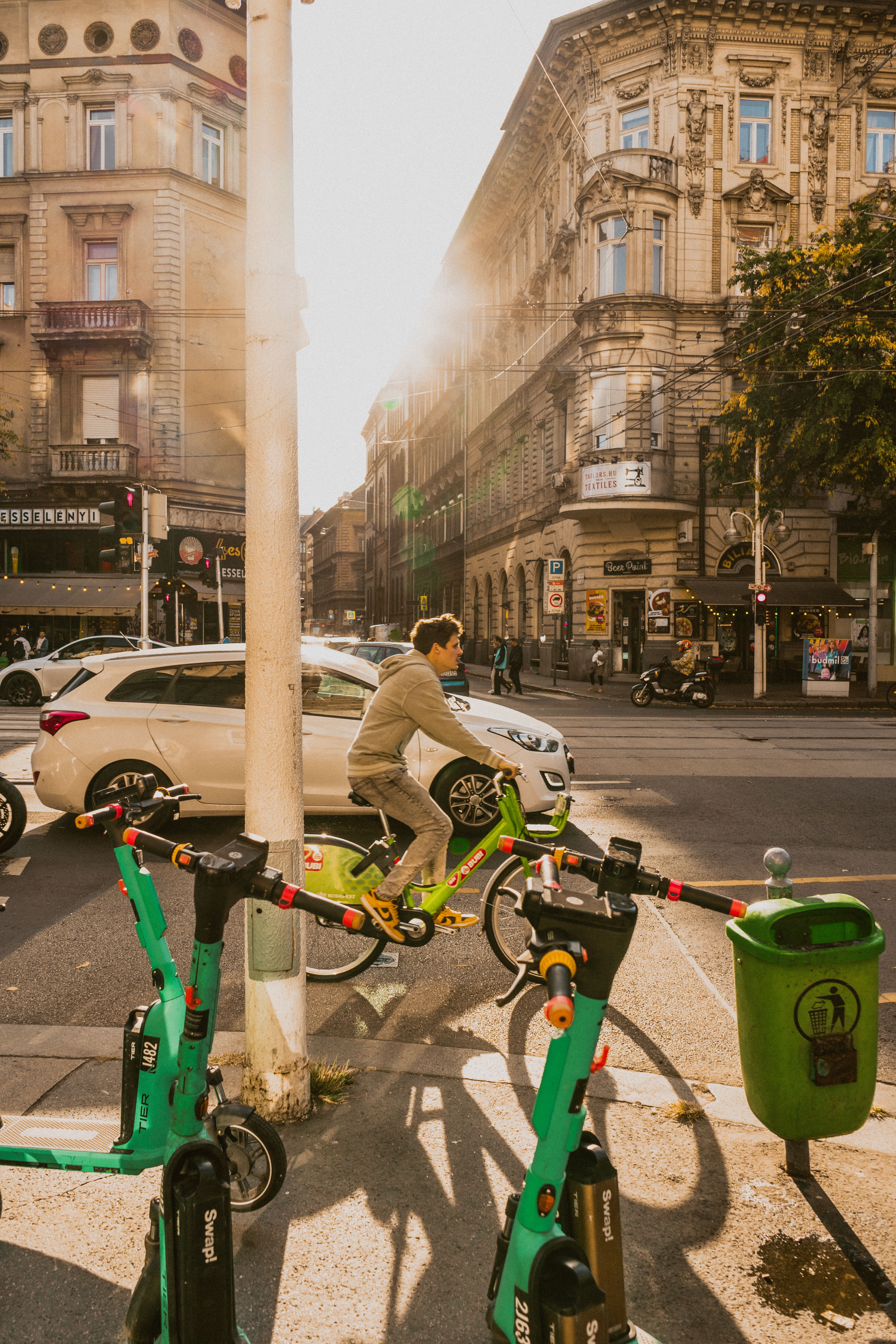 Urban scene with a cyclist in Budapest, Hungary, amidst vibrant architecture and electric scooters.