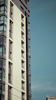 Tall modern apartment building with glass windows against a clear blue sky.