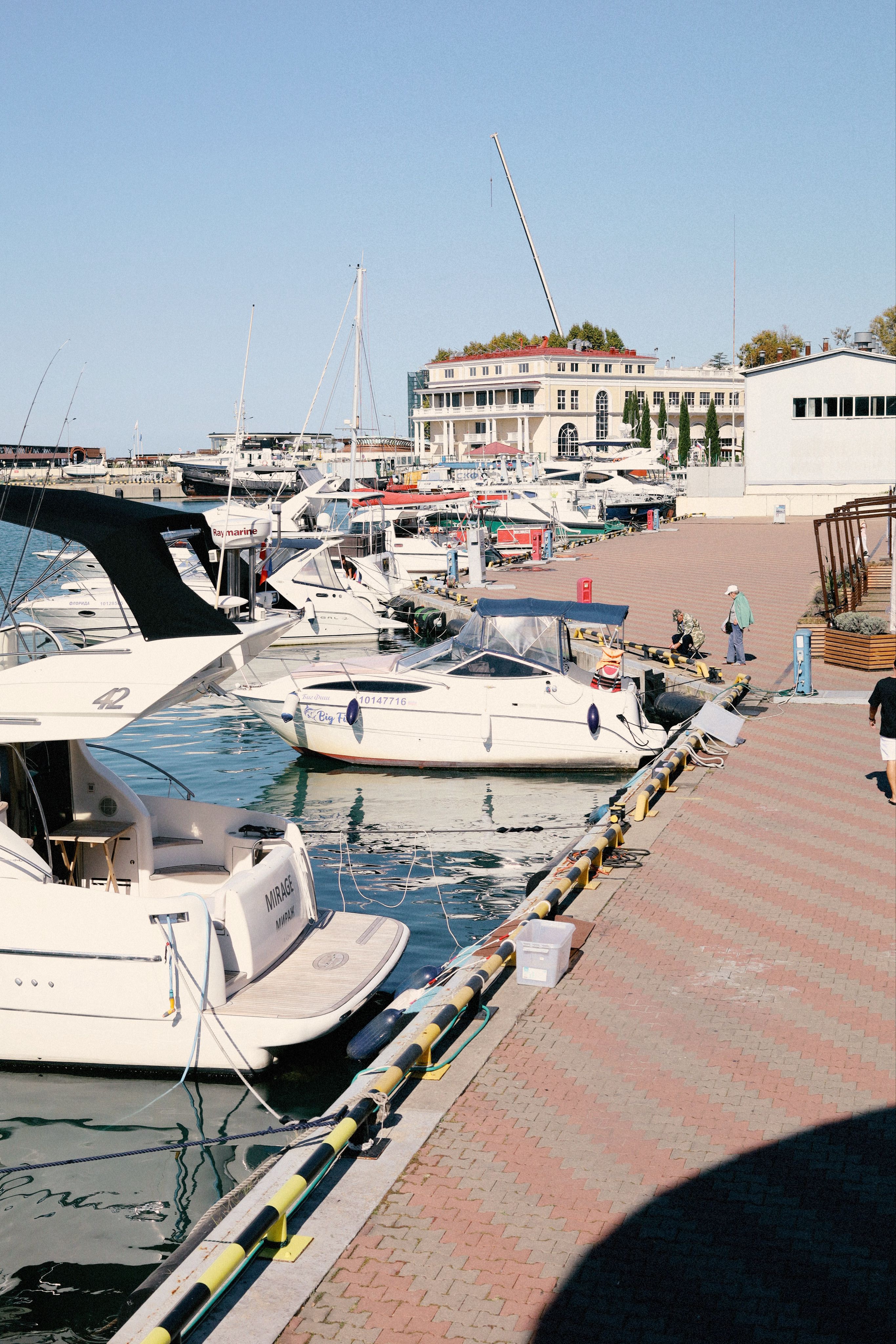 A vibrant marina scene featuring yachts docked near a waterfront promenade under a clear blue sky.
