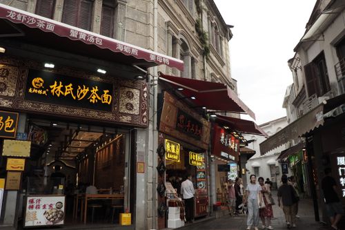 Free Lively street market scene with people walking past vibrant Asian shops. Stock Photo