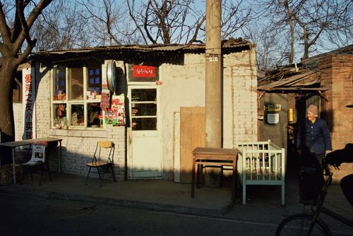 Free A small rustic street market with an elderly woman standing outside under daylight. Stock Photo