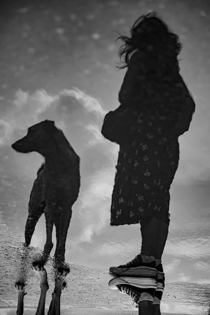 Artistic reflection of a woman and dog in water creating a surreal effect.