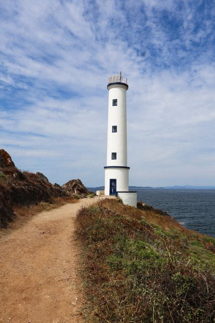 White lighthouse on a rocky coastal path under a vibrant blue sky.