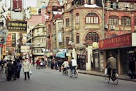 一条繁忙的城市街道上，人们步行或骑自行车经过历史建筑和色彩缤纷的标志