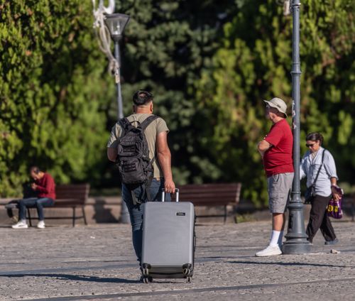 Free A man with a suitcase and backpack strolling in a sunny park in İzmir, Türkiye. Stock Photo