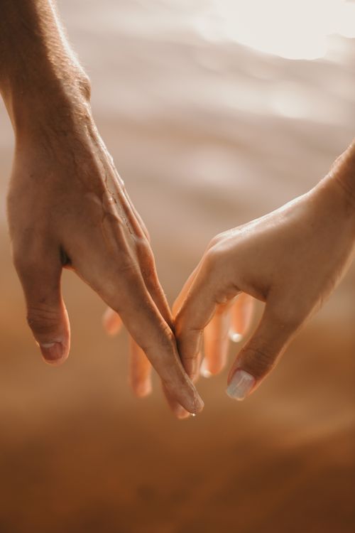 Free A close-up of a couple holding hands with a romantic sunset in the background. Stock Photo