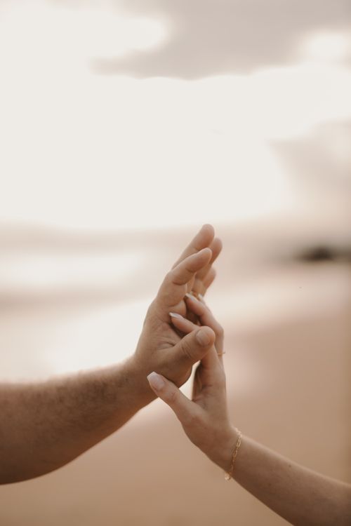 Free Close-up of hands touching gently at a beach during sunset, evoking warmth and connection. Stock Photo