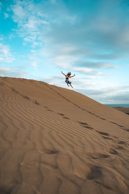 Free Person jumping on a large sand dune under a clear blue sky. Stock Photo