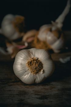 Moody close-up of fresh garlic bulbs on a rustic wooden table.