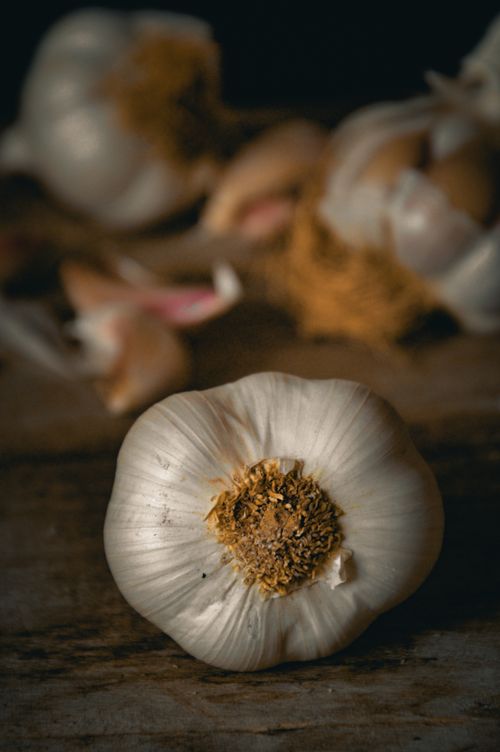 Free Detailed close-up of a garlic bulb on a rustic table with a dark, moody background. Stock Photo