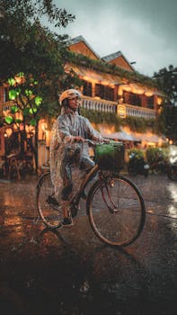 A person rides a bicycle in the rain at night, passing a traditional illuminated building.