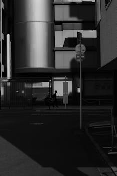 Black and white urban street scene with modern architecture and dramatic shadows.