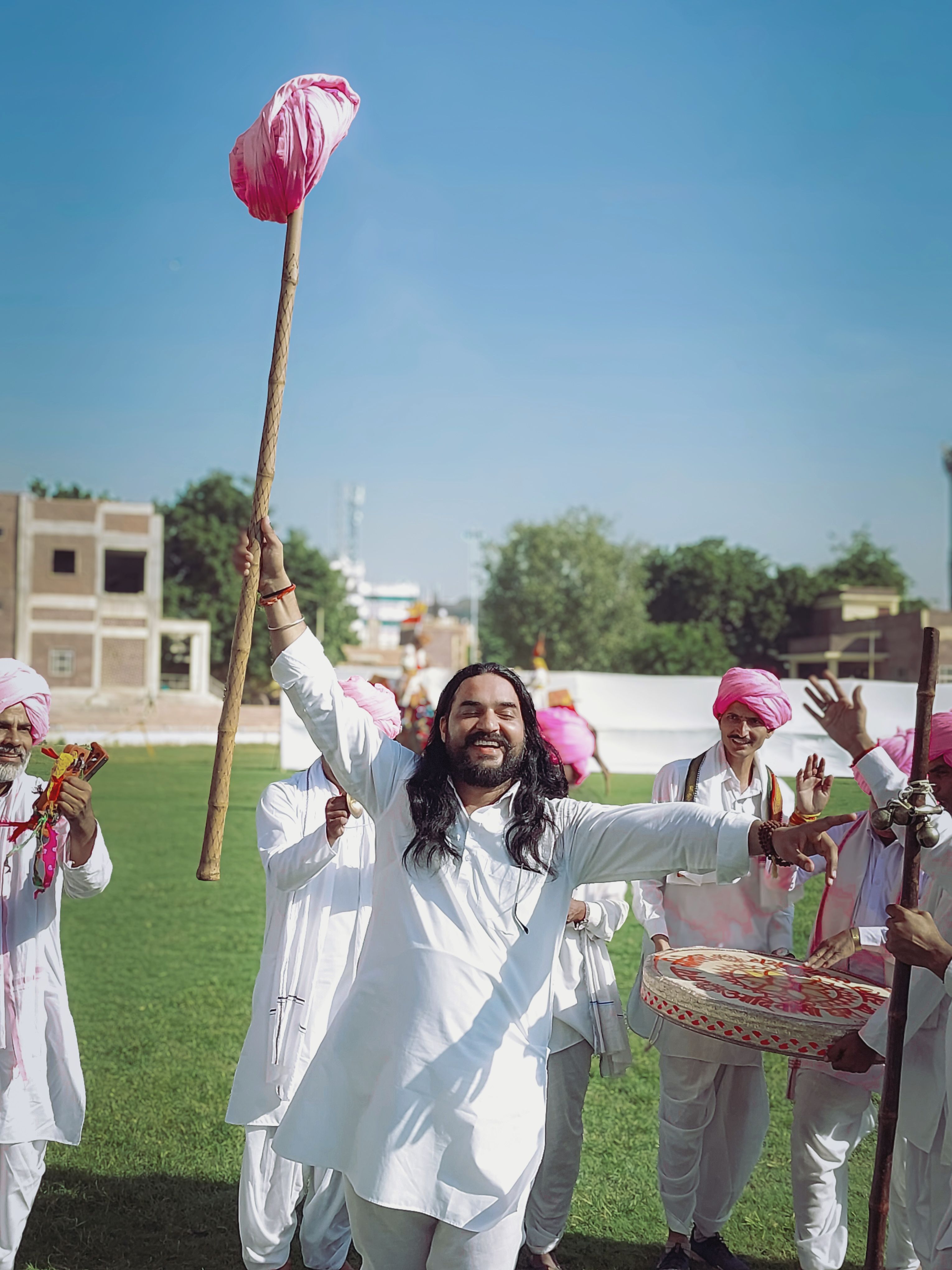 Group of men in traditional attire celebrating outdoors with music and dance.