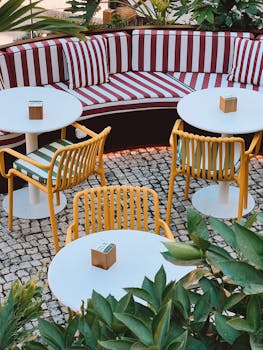 Vibrant outdoor cafe with striped cushions and yellow chairs, surrounded by greenery.