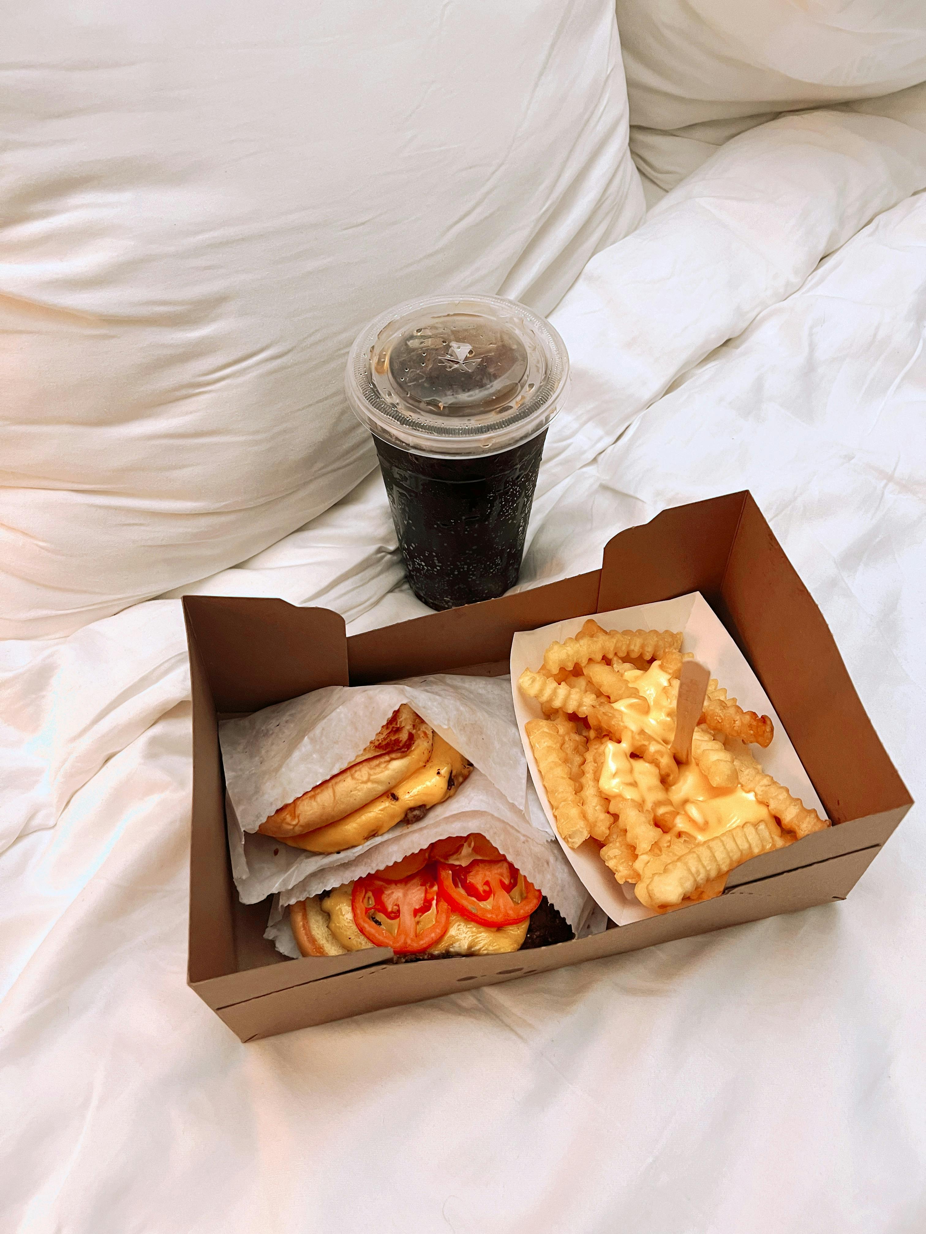 Box with a sandwich and crinkle-cut fries, drink on bed.