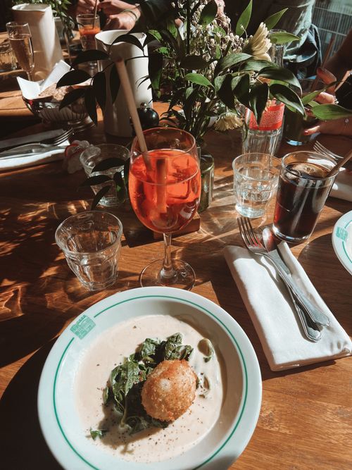 Free Sunlit brunch with Aperol Spritz, salad, and vibrant decor on a wooden table. Stock Photo