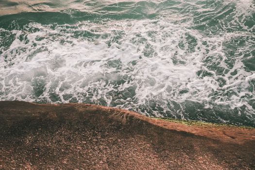 An aerial view of waves crashing against a rocky shore, capturing the ocean's dynamic movement.