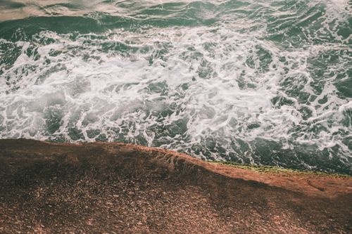 Free An aerial view of waves crashing against a rocky shore, capturing the ocean's dynamic movement. Stock Photo