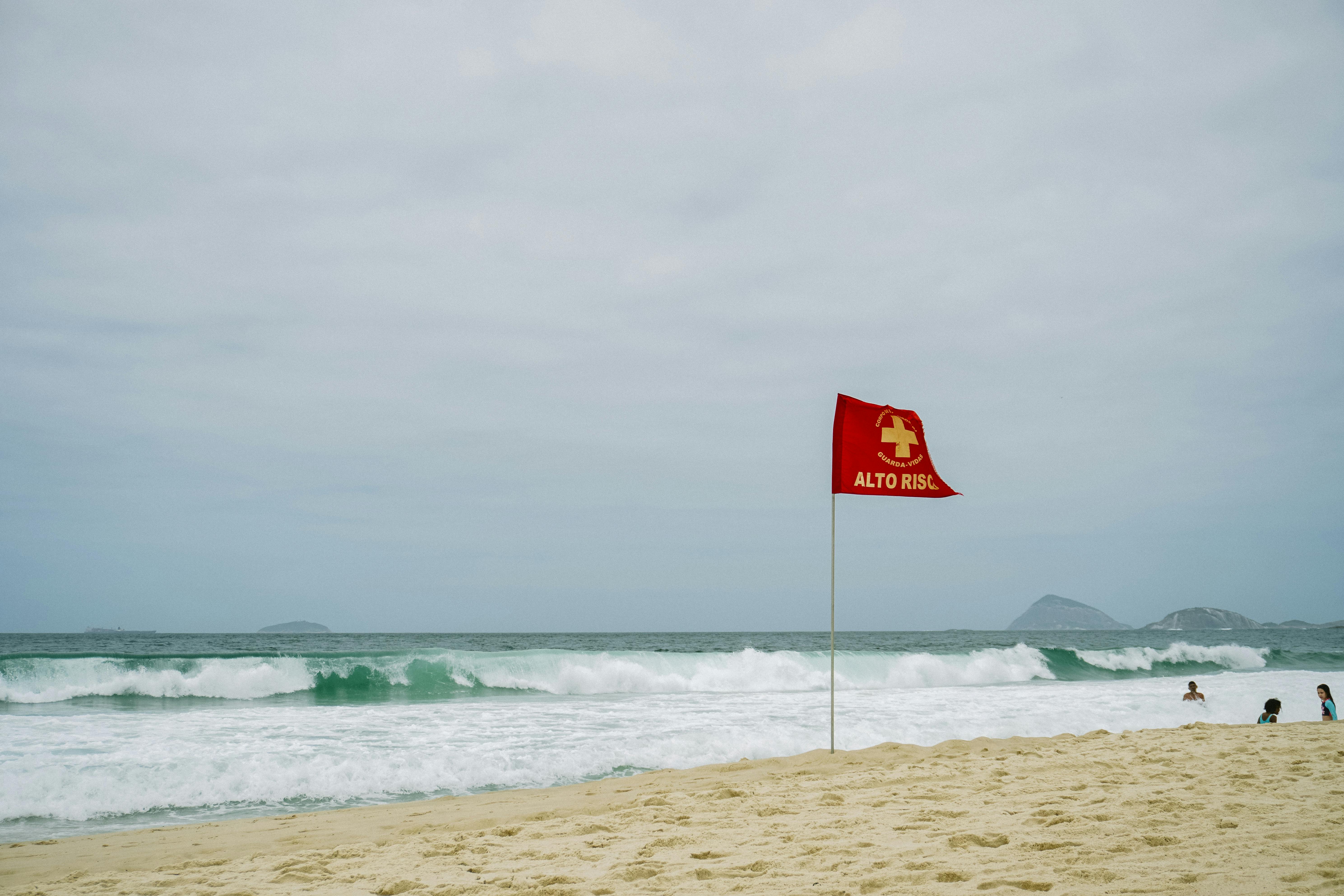 High-risk warning flag on a sandy beach with ocean waves and distant islands.