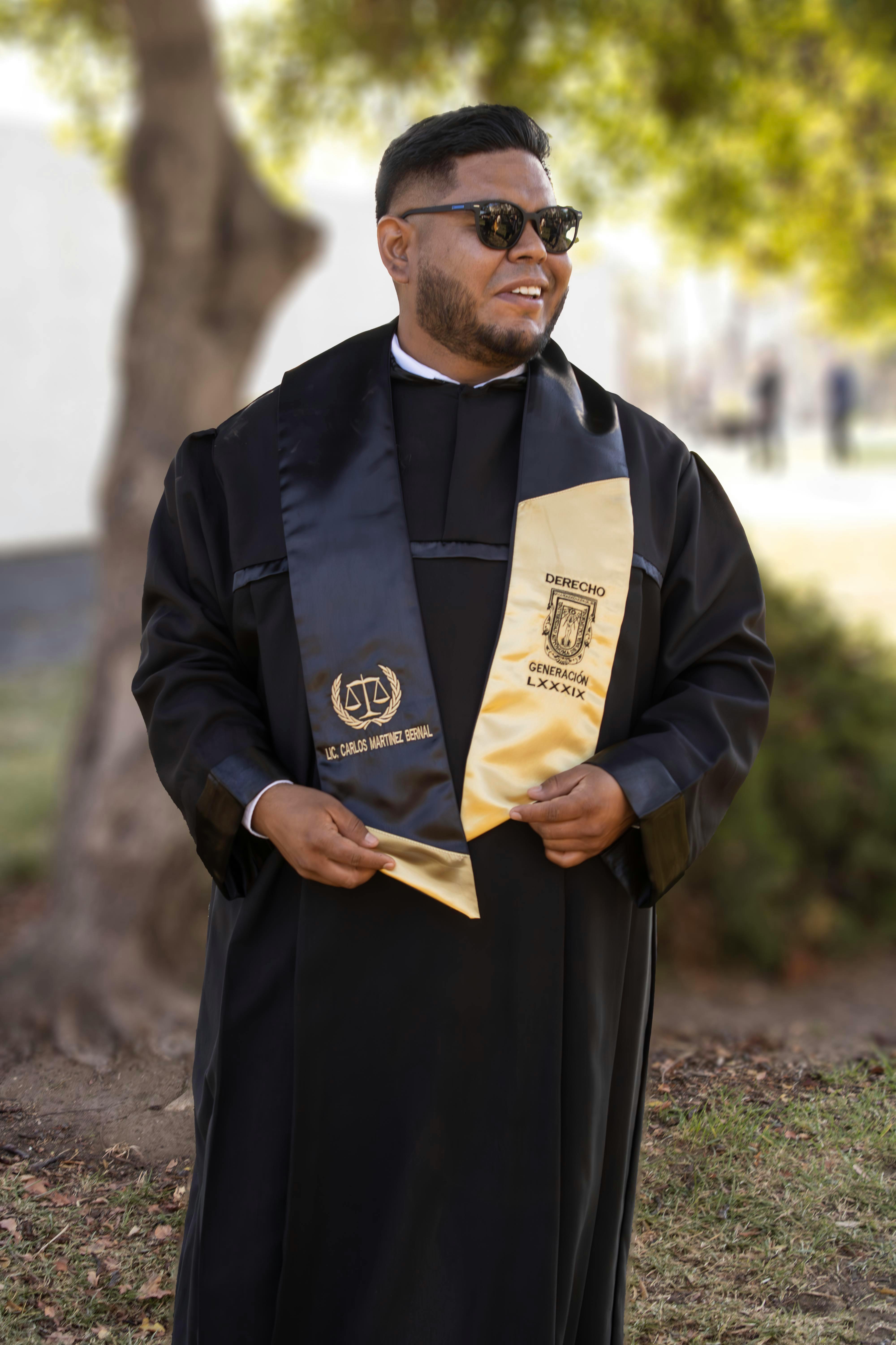 A law graduate in ceremonial attire celebrates graduation outdoors with joy and pride.