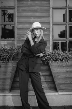 Elegant woman in suit and hat posing outdoors against rustic background.