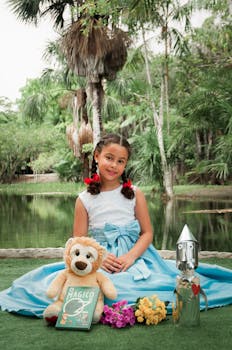 一个穿着蓝色连衣裙的可爱女孩在宁静的湖边微笑着，身边摆着玩具和鲜花