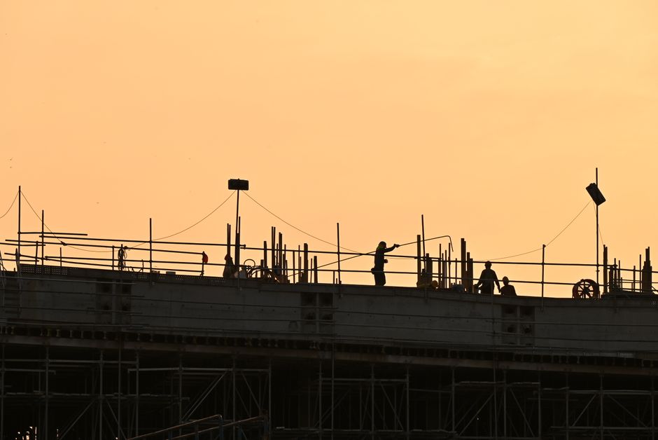 Silhouetted workers on a construction site against a warm sunset sky.