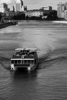 Black and white photo of a river boat cruising on the Moscow River with cityscape in the background.