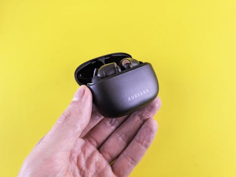 Close-up of a hand holding a black Aurvana wireless earbuds case against a vibrant yellow background.