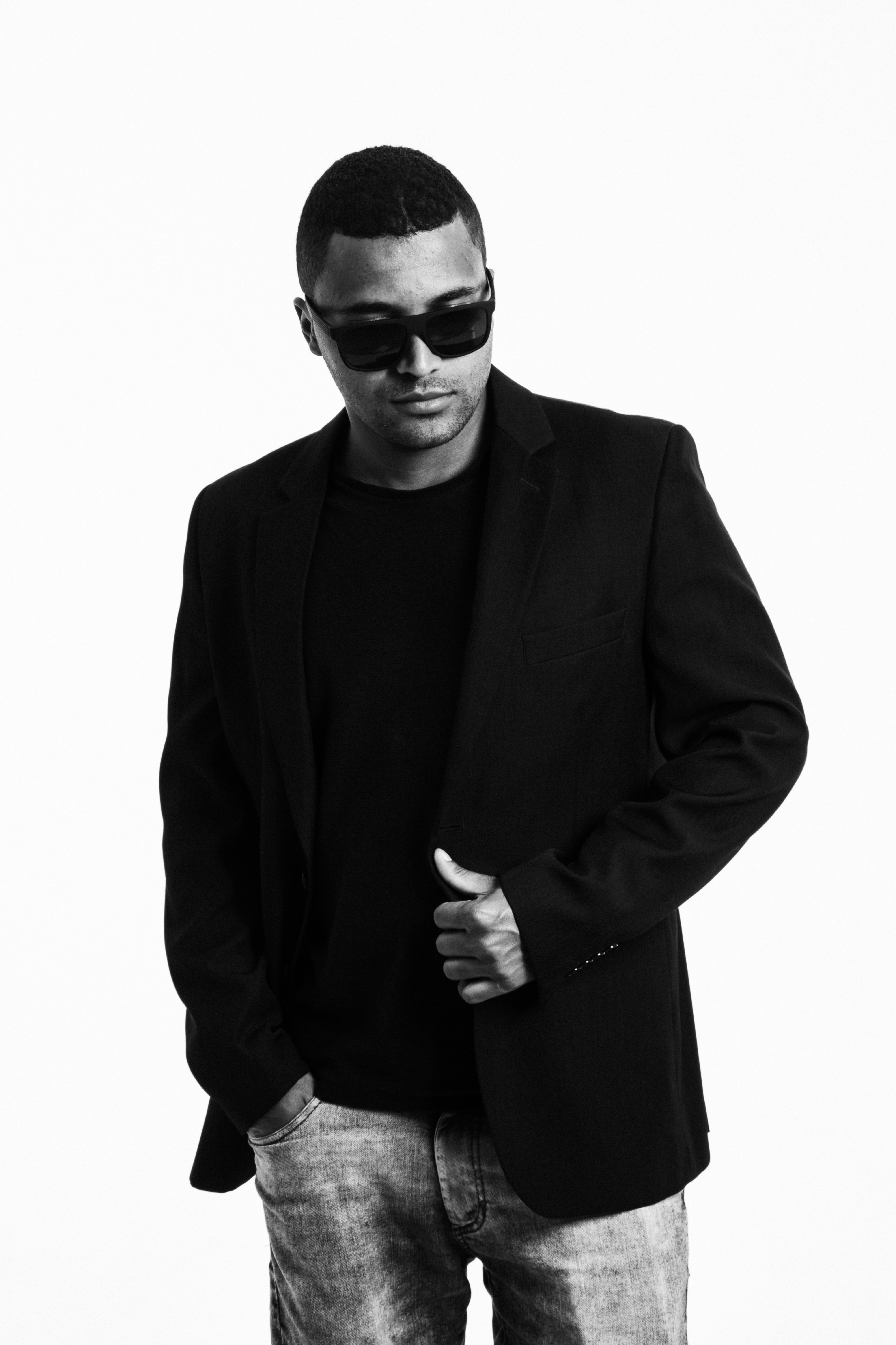 Black and white portrait of a stylish man in sunglasses and blazer, exuding confidence.