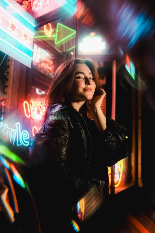 Free Young woman posing confidently under colorful neon lights, creating a vibrant night scene. Stock Photo