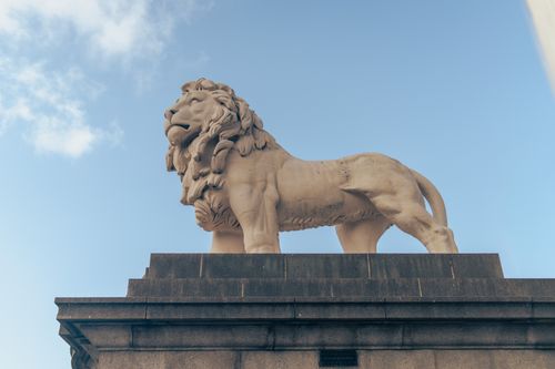Free Majestic lion statue atop a pedestal against clear blue sky in London, England. Stock Photo