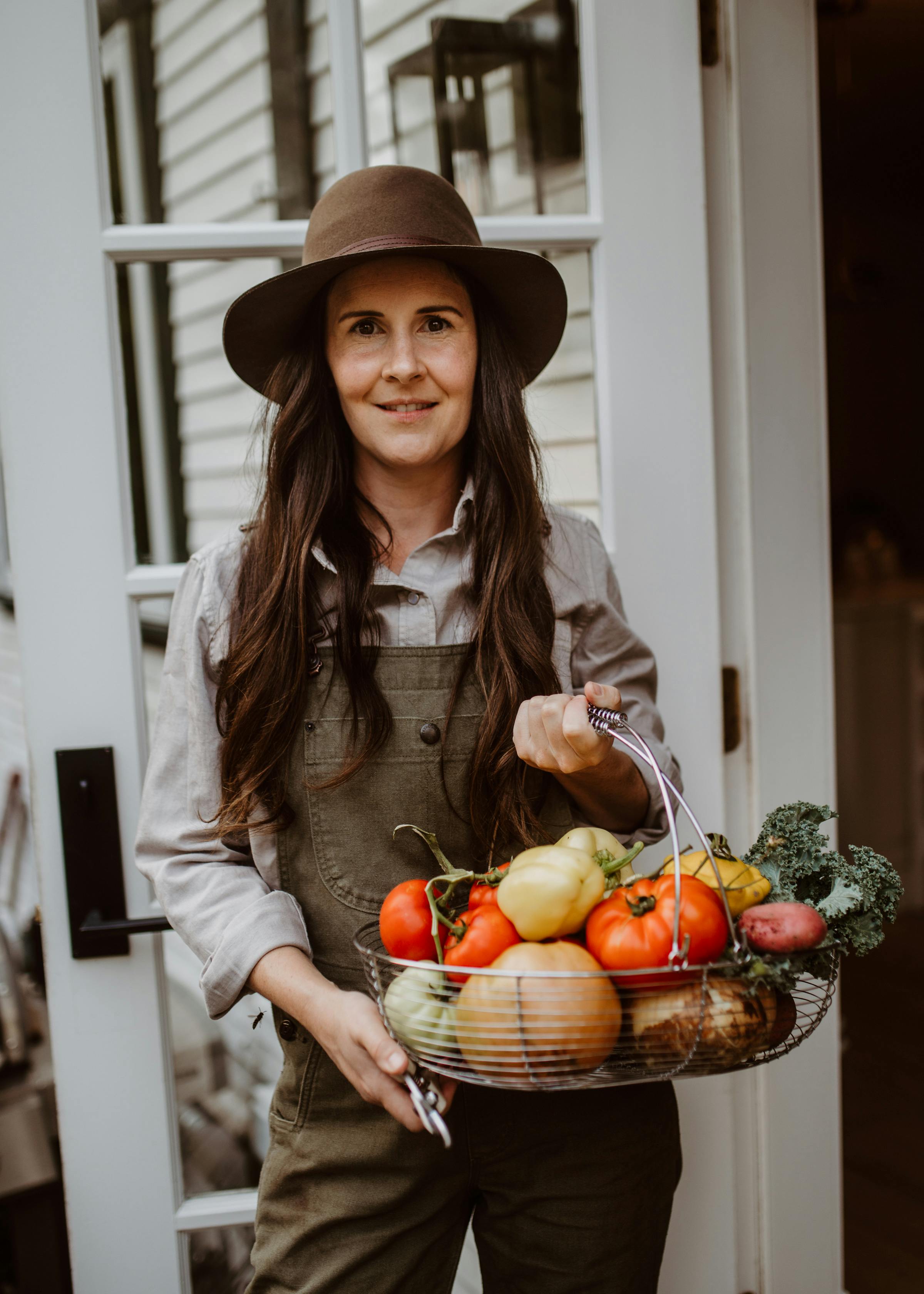 Smiling woman stands with a harvest basket of fresh vegetables in an autumn garden.