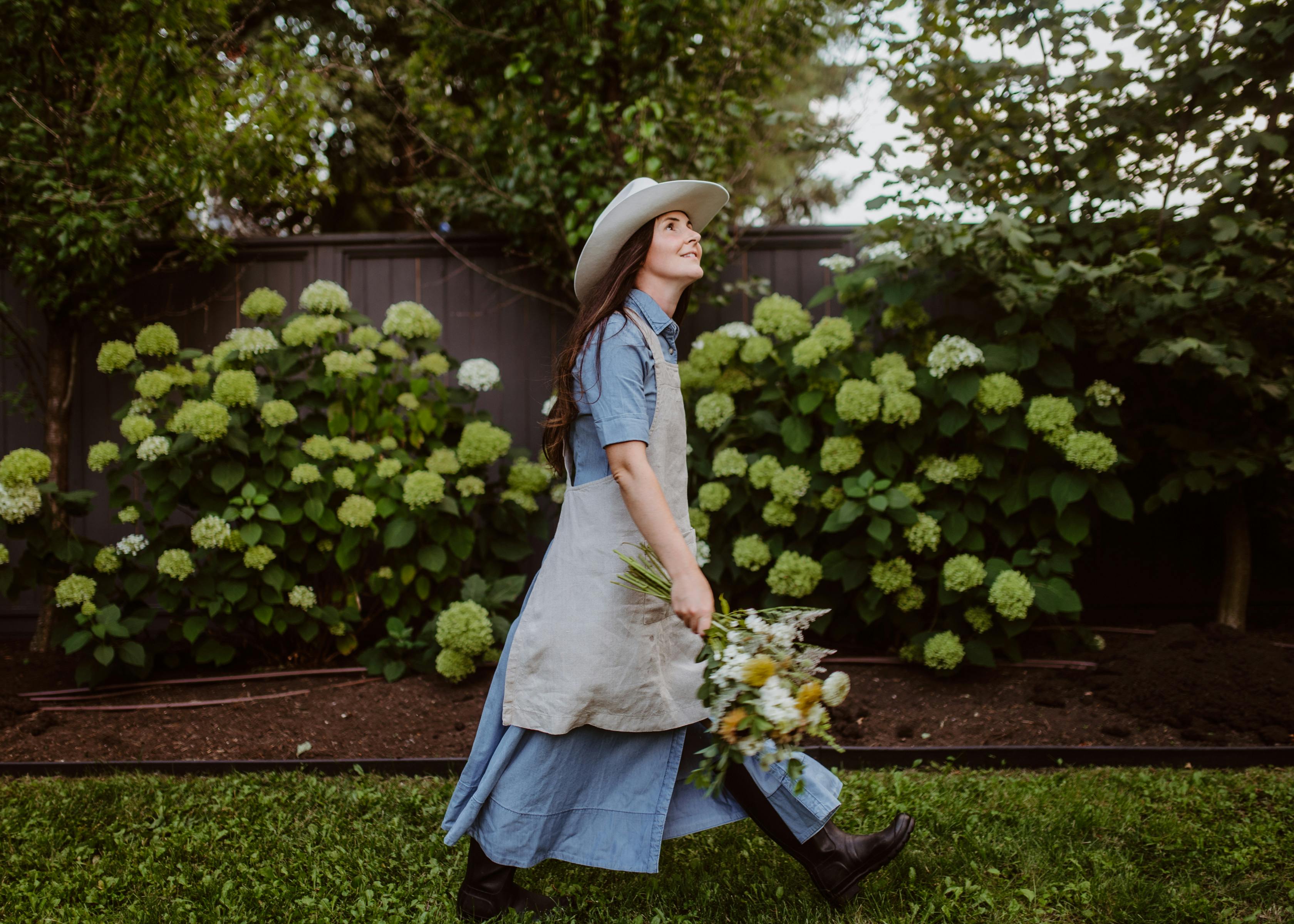 Gardener in denim dress with linen apron walking by hydrangeas
