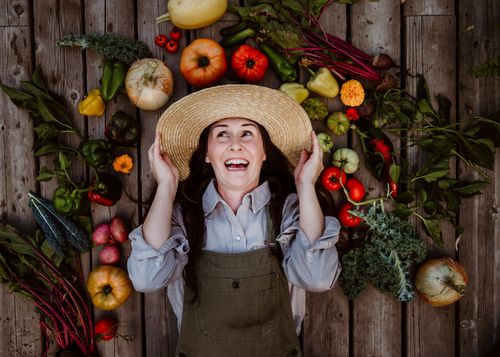 Free Happy woman gardener surrounded by a rich variety of fresh autumn vegetables, celebrating harvest on a rustic wooden background. Stock Photo