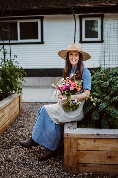 Free Woman in denim dress and straw hat holding pink flowers in a home garden. Stock Photo