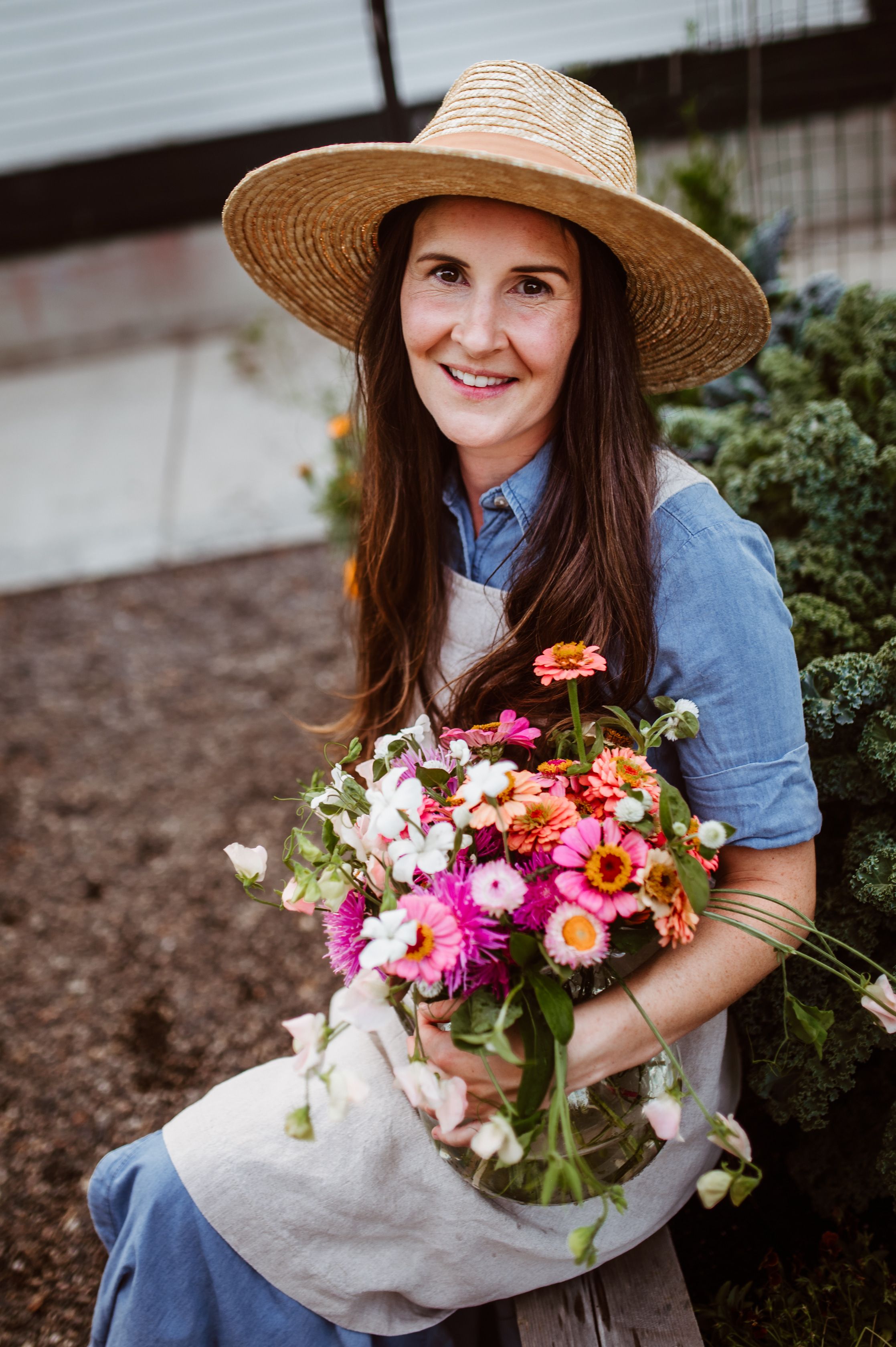 Woman in a straw hat holding bright flowers in a summer garden.